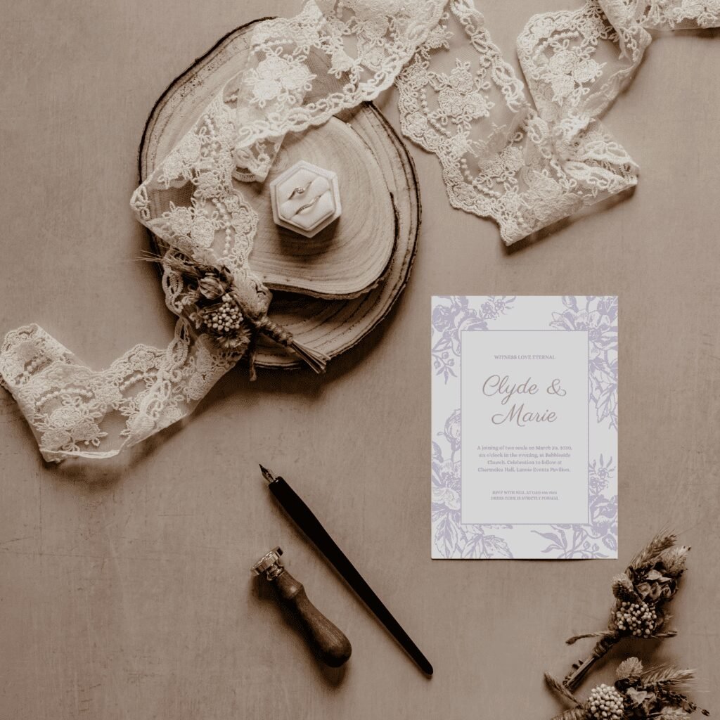 A flat lay of a wedding invitation reading Clyde & Marie, surrounded by lace, dried flowers, a pen, a wax seal stamp, wooden slices, and a ring box with two rings—a perfect inspiration for modern wedding trends—arranged on a beige surface.